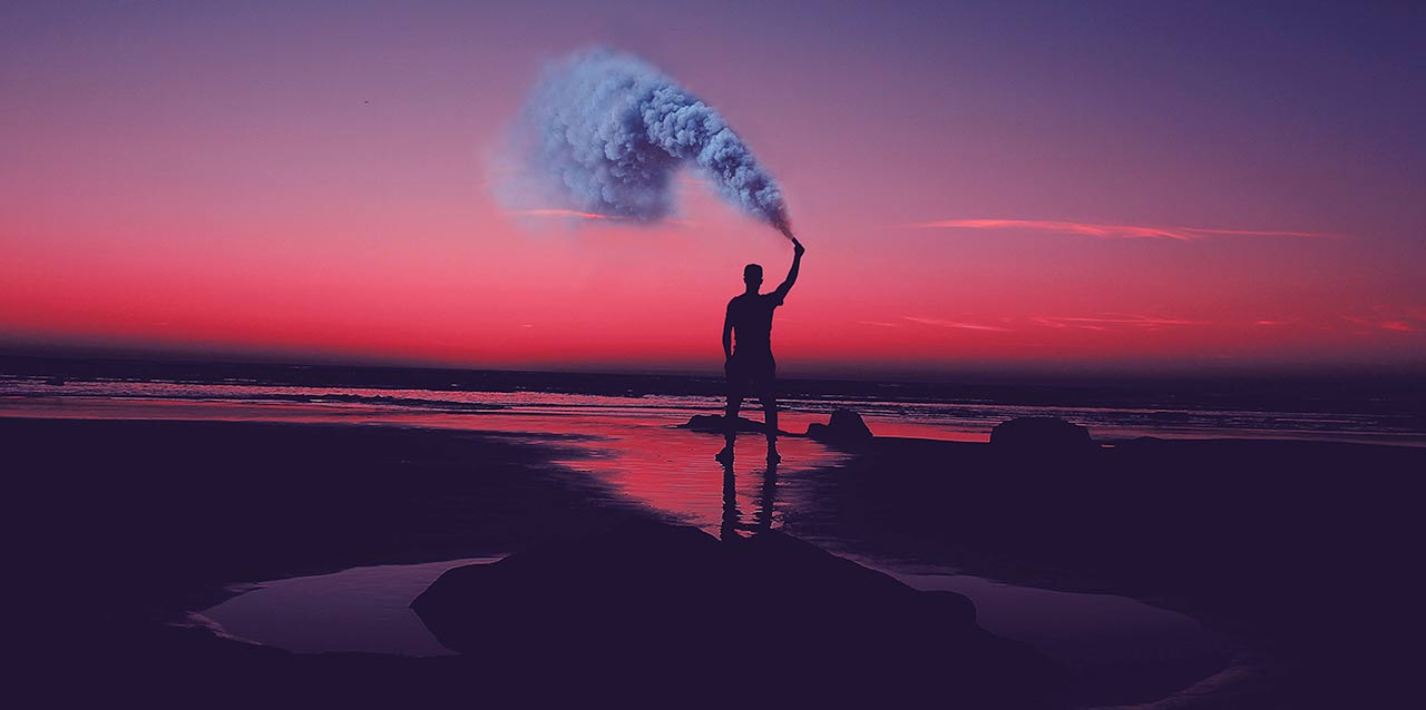 homem a segurar bengala de fumo junto ao mar