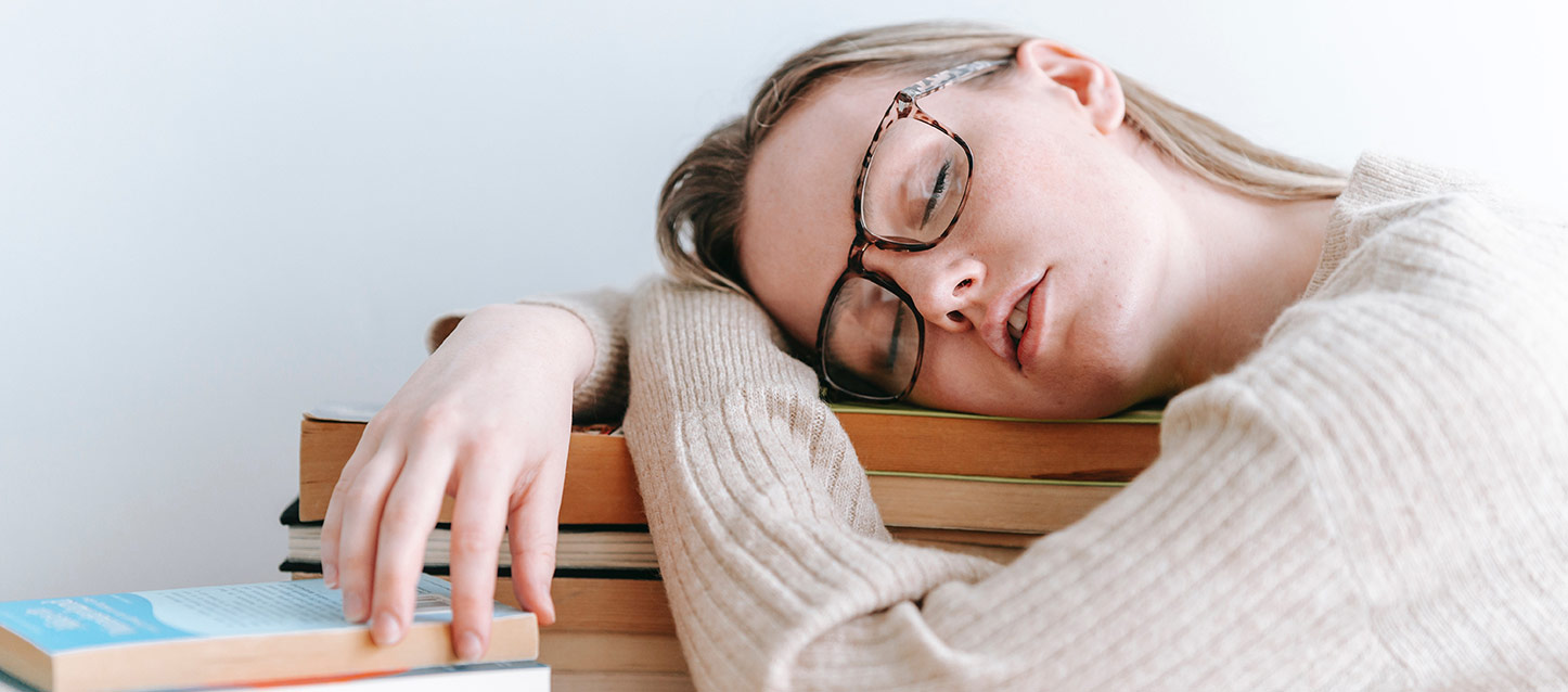 rapariga de cabelo loiro, com óculos grandes, a dormir sobre uma pilha de livros