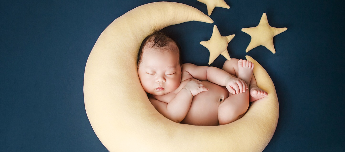 bebé sem roupa a dormir sobre um colchão com forma de lua e estrelas