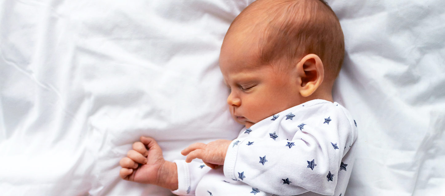 bebé a dormir de lado, com um pijama branco e estrelas azuis