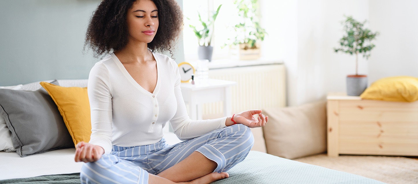 rapariga morena de cabelo afro, a meditar sentada em cima da cama