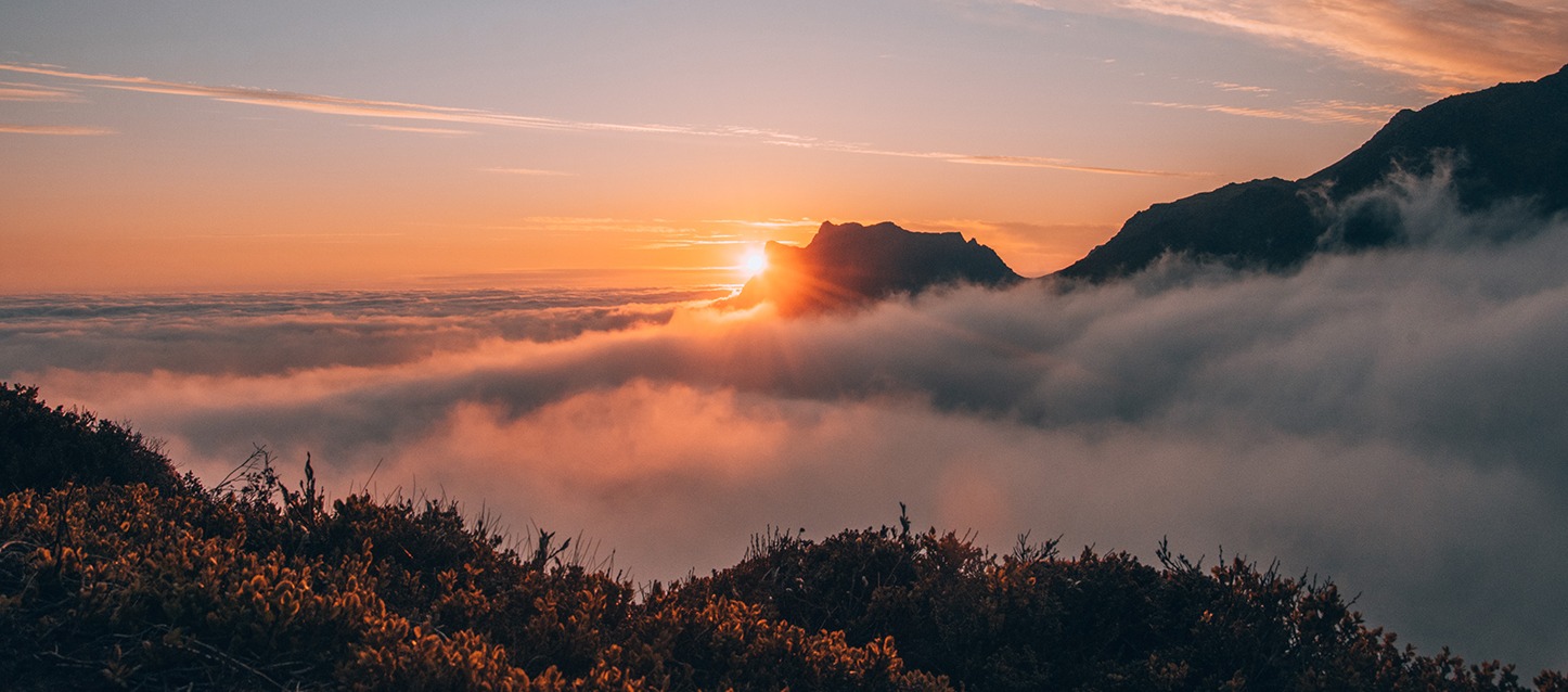 sol de meia-noite, com o sol a assomar por uma montanha, visto de grande altura e com nuvens à volta