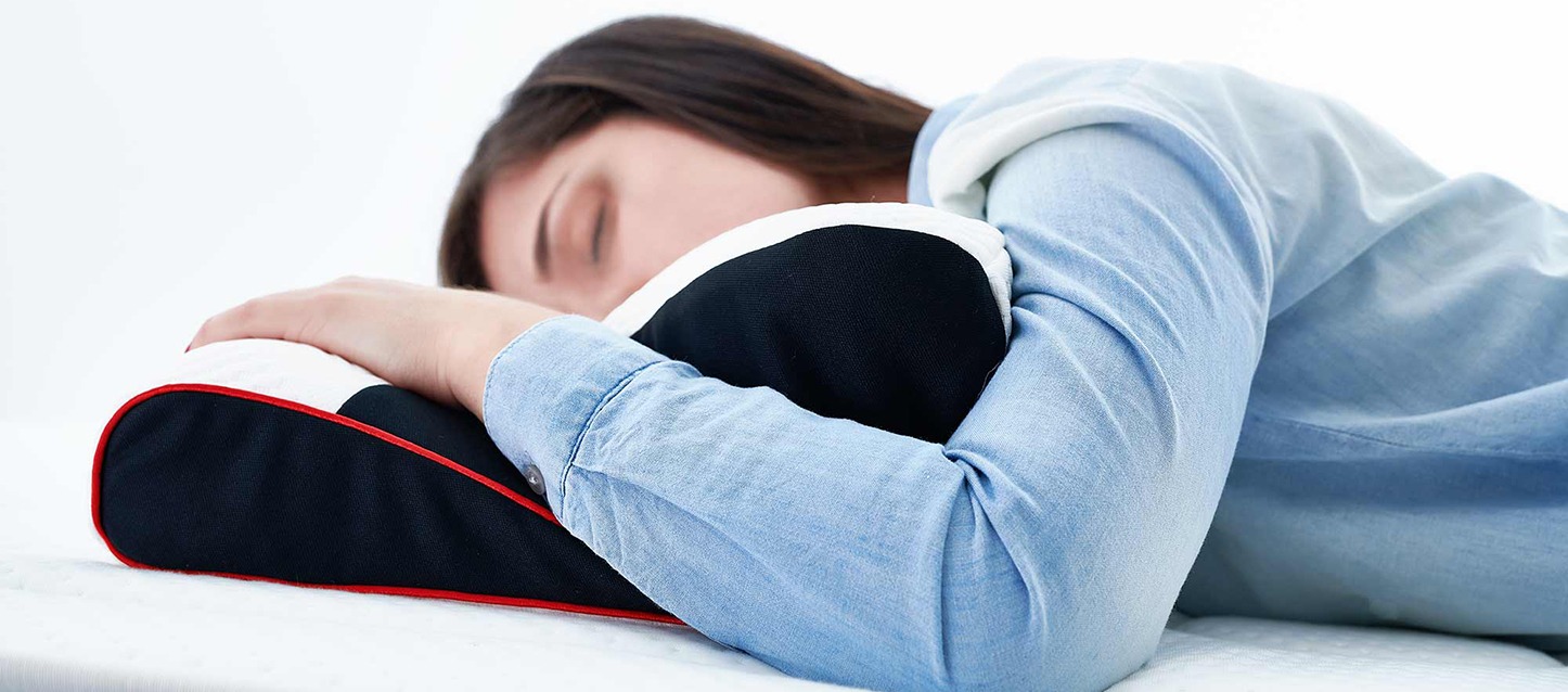 rapariga com dor cervical a dormir de barriga para baixo, com uma almofada cervical