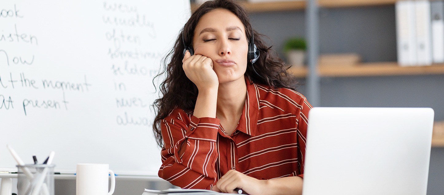 rapariga morena de cabelo comprido e ondulado, com camisa vermelha e riscas brancas, com auriculares, dormida por narcolepsia, com a mão apoiada no queixo, em frente ao computador