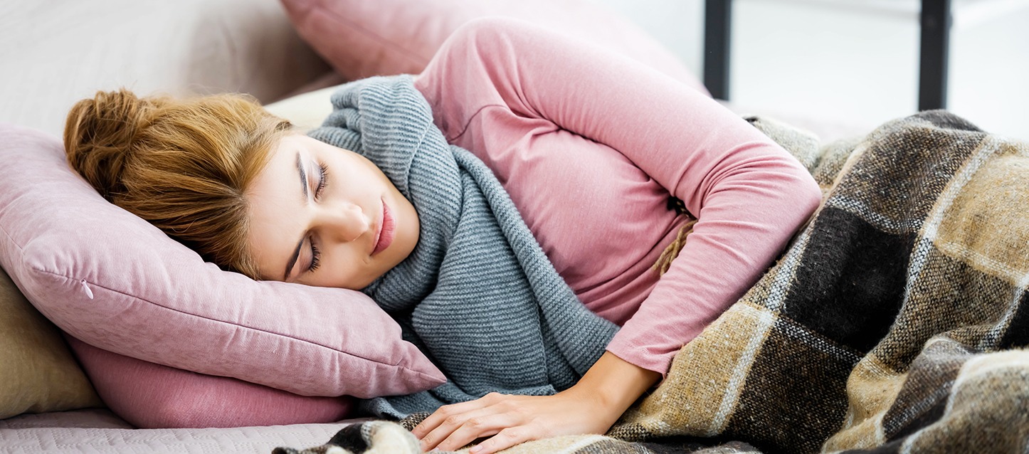 rapariga loira com pijama rosa e cachecol, a dormir de lado e tapada com manta aos quadrados castanhos e pretos