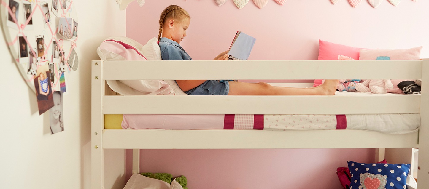 uma menina loira com tranças a ler um livro na cama de cima de um beliche