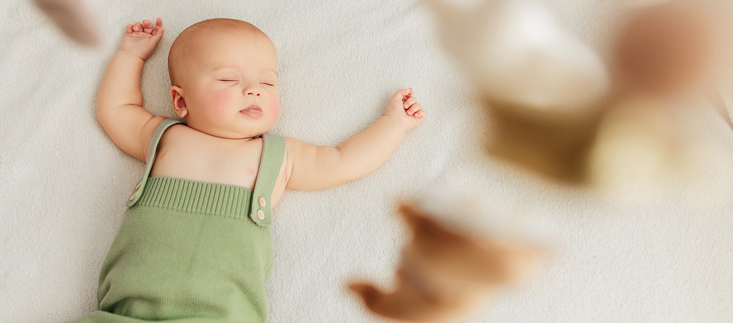 bebé a dormir de barriga para cima, com pijama de alças verde, e com os braços estendidos.