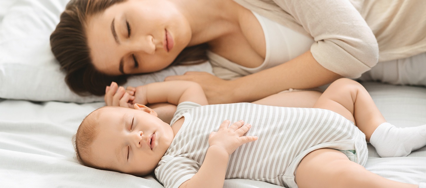 mulher a dormir de lado na cama, junto ao seu bebé na cama