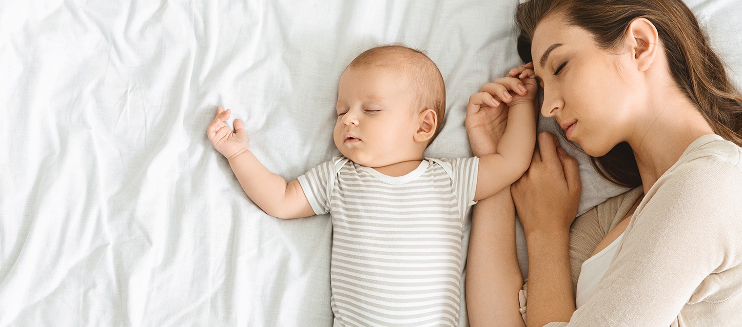mãe a dormir na cama de lado junto ao seu bebé dormido