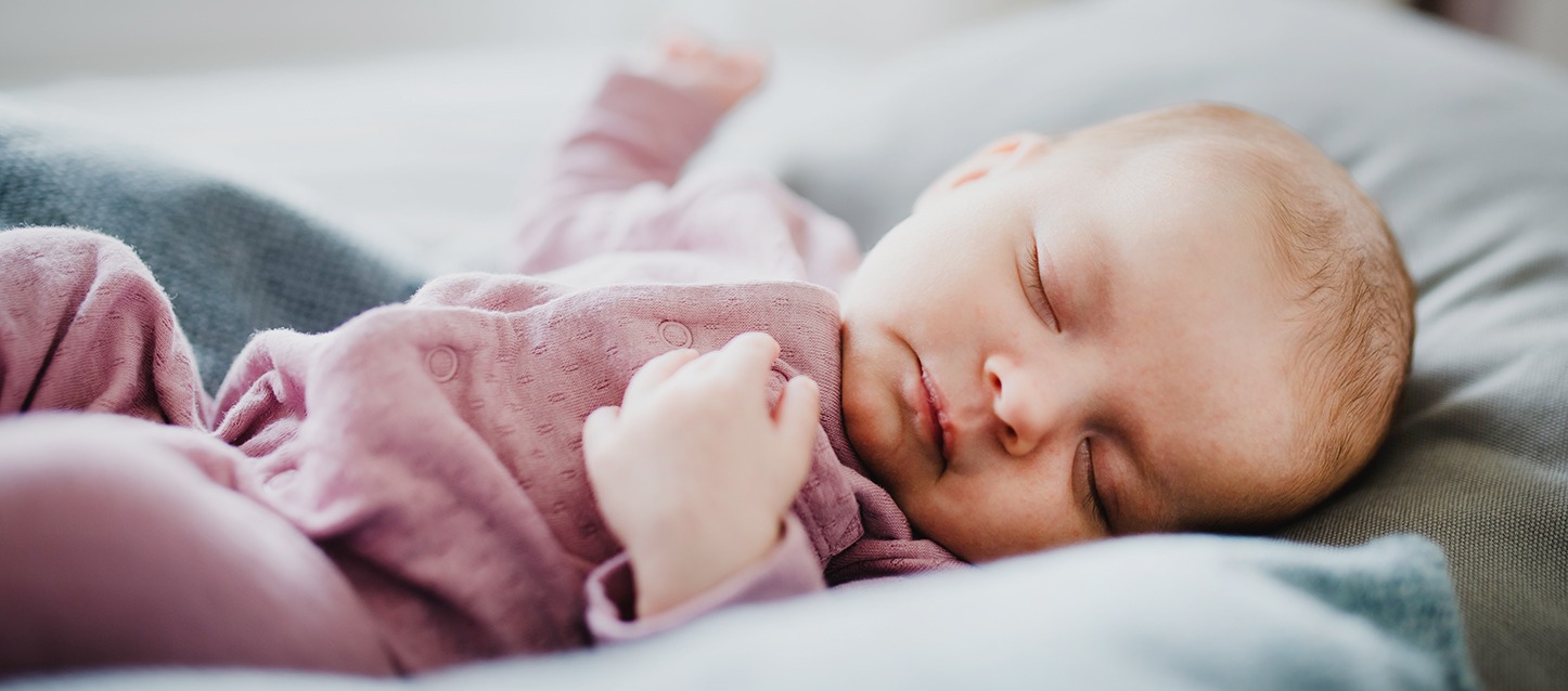 bebé dormido de barriga para cima, com um pijama roxo