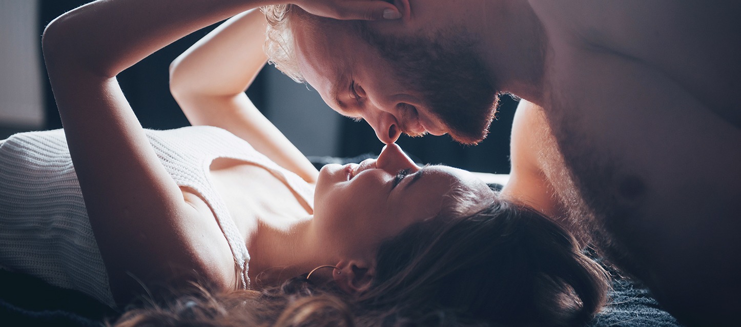 casal em atitude carinhosa em cima da cama, unindo as pontas do nariz de modo afetuoso