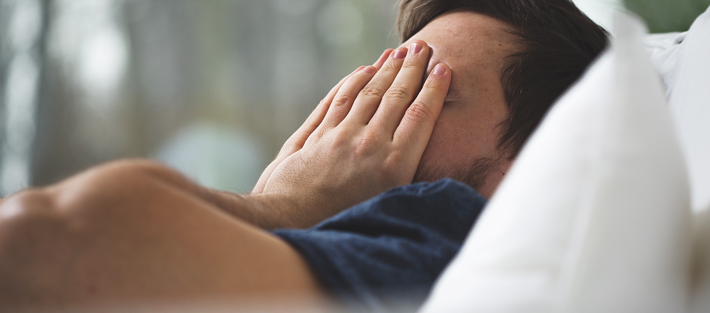 rapaz metido na cama, de barriga para cima, com as mãos na cara