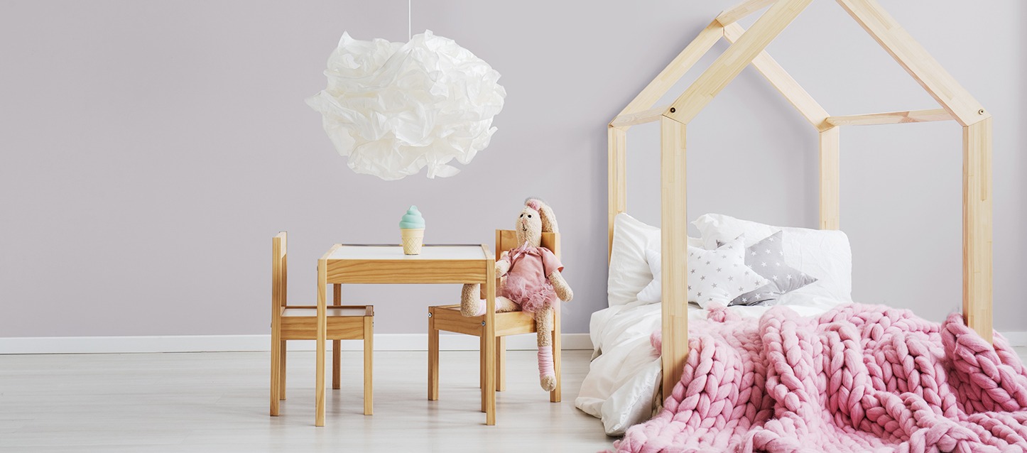 cama montessori com forma de casa, travesseiros com forma de estrela, cobertor de malha, e mesa e duas cadeiras, com um coelho de peluche sentado numa