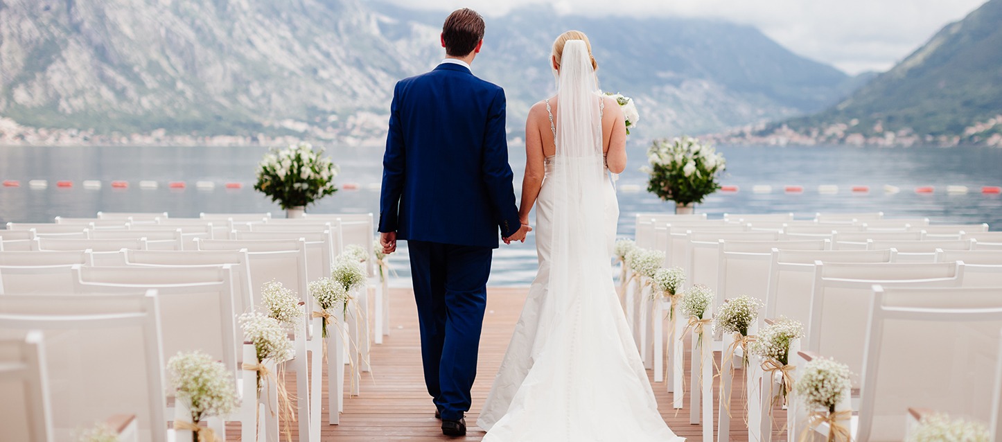 casal de namorados a caminhar por uma plataforma de madeira rodeada de assentos, ao ar livre e em frente ao mar