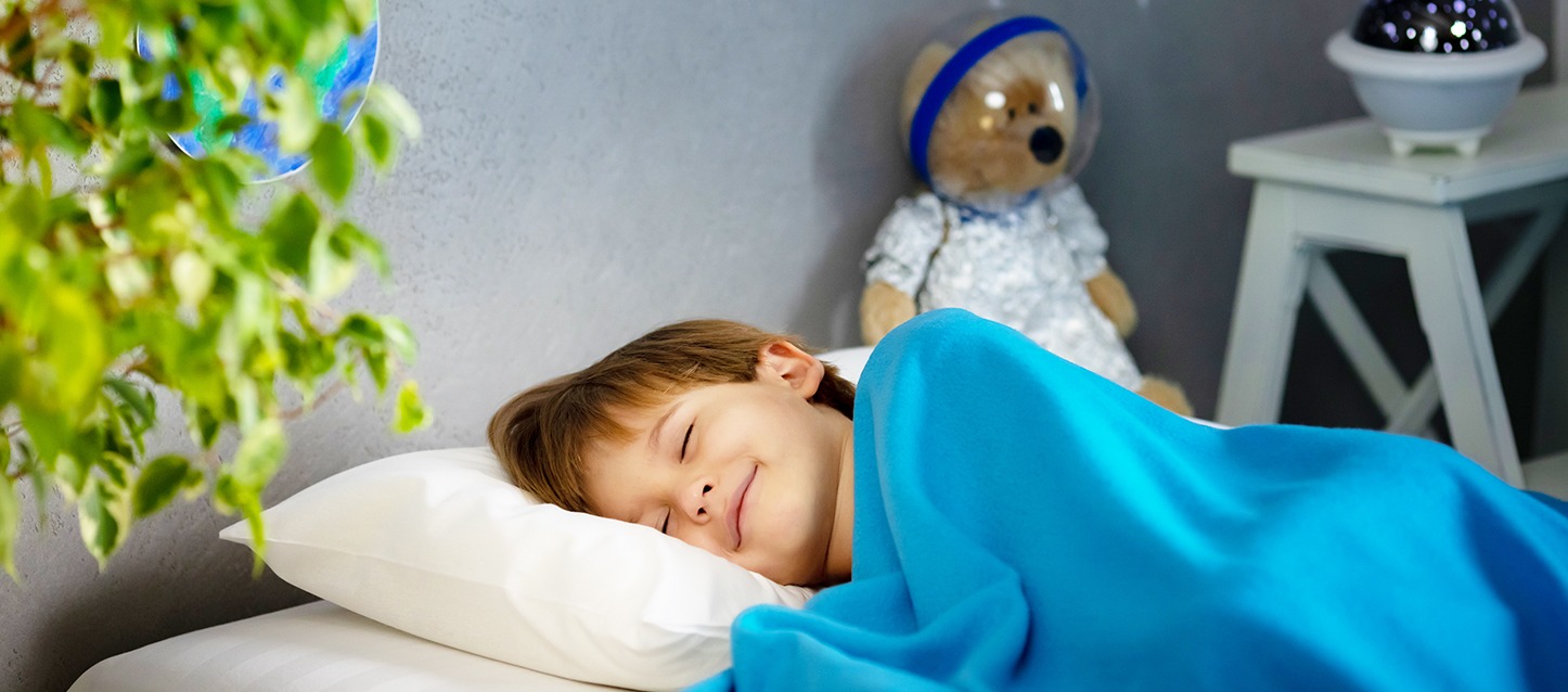 menino a dormir de lado sorrindo, tapado com uma manta azul