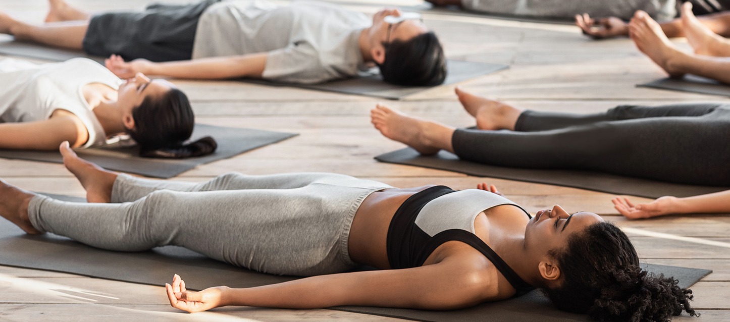 várias pessoas deitadas de barriga para cima sobre um tapete, a praticar yoga nidra