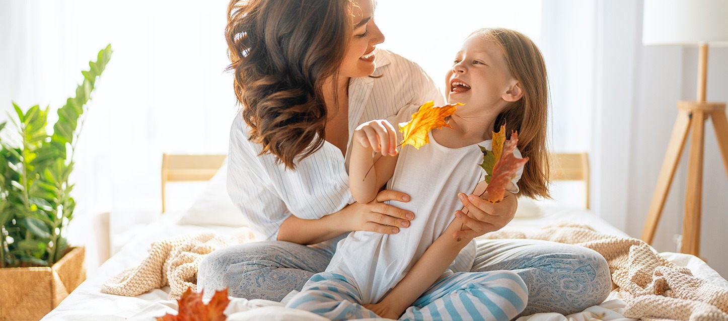 uma mãe a brincar com a sua filha, sentadas na cama com folhas secas de outono