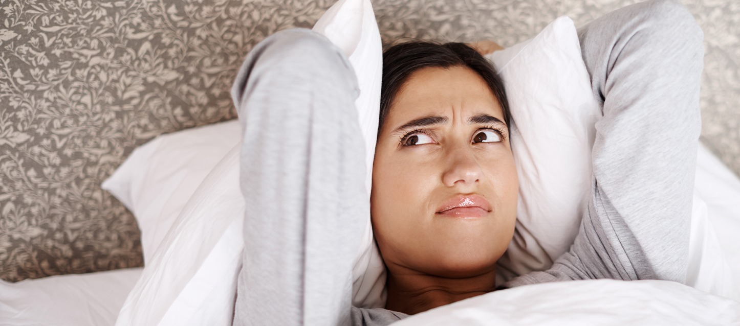Mulher metida na cama a olhar para o teto com gesto de desaprovação.