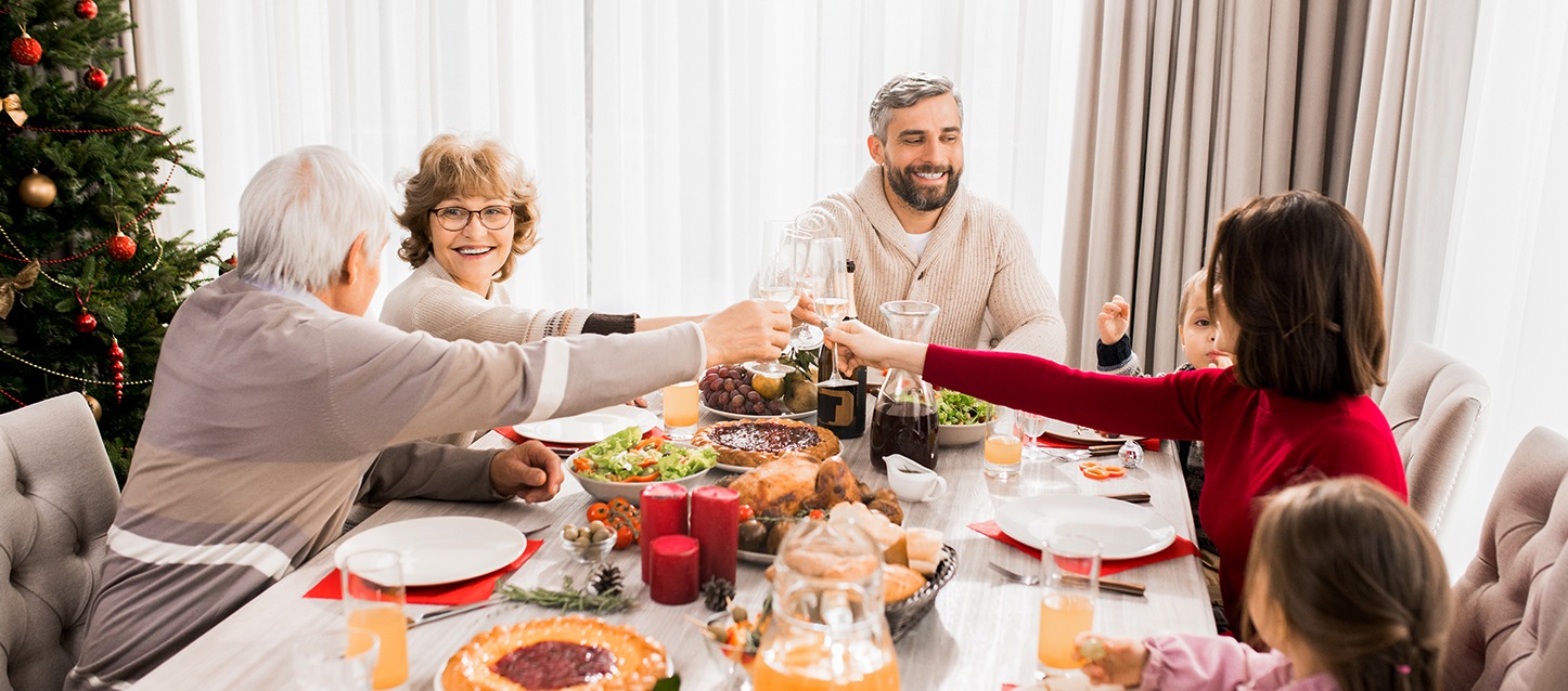 Comida familiar com dois avós, dois pais e duas crianças, onde os adultos estão a brindar.